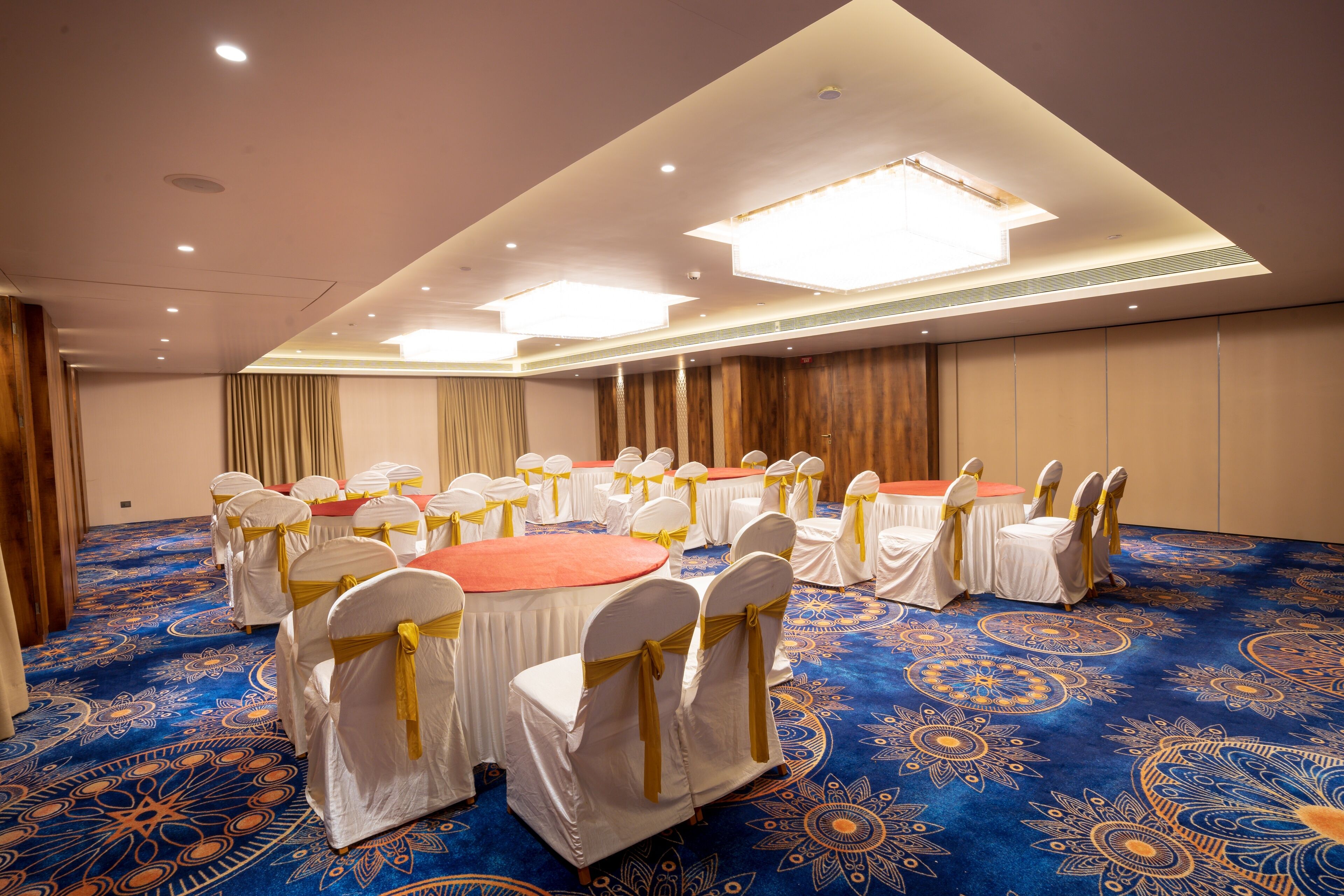 A conference room with round tables and white chairs, carpeted floor, and ceiling lights.