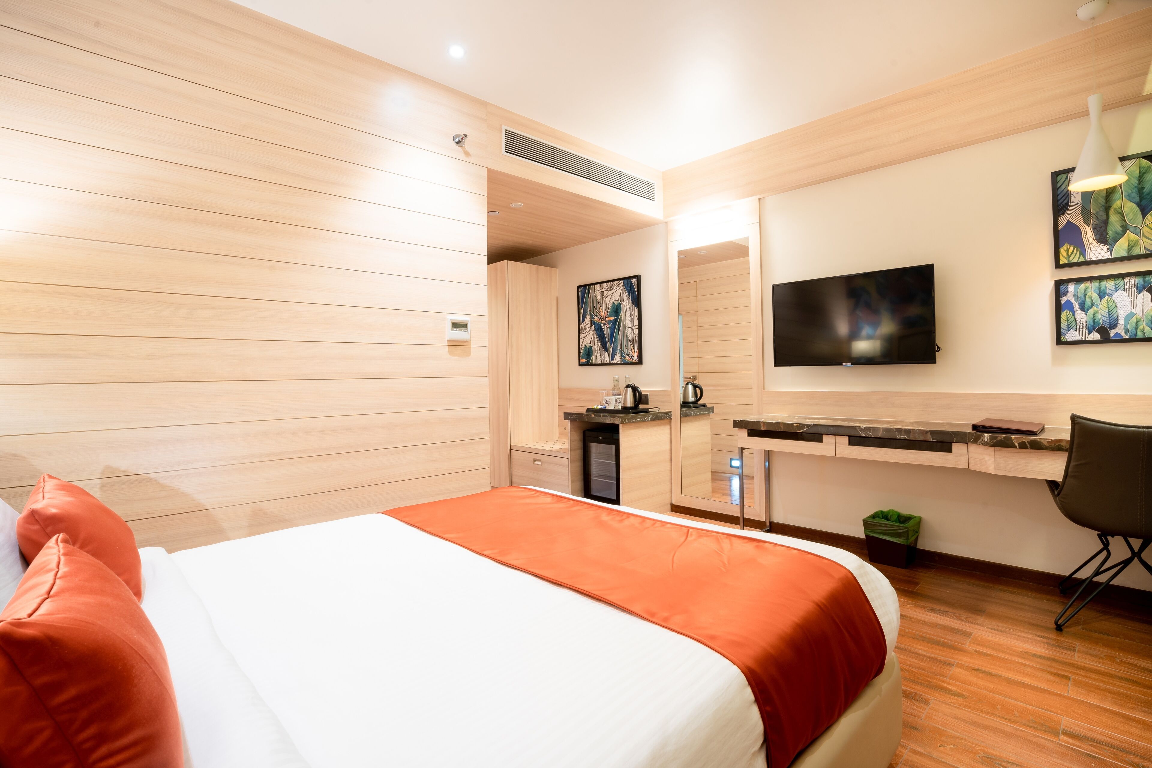 A hotel room with a bed, a desk, a television, and artwork on the wall.