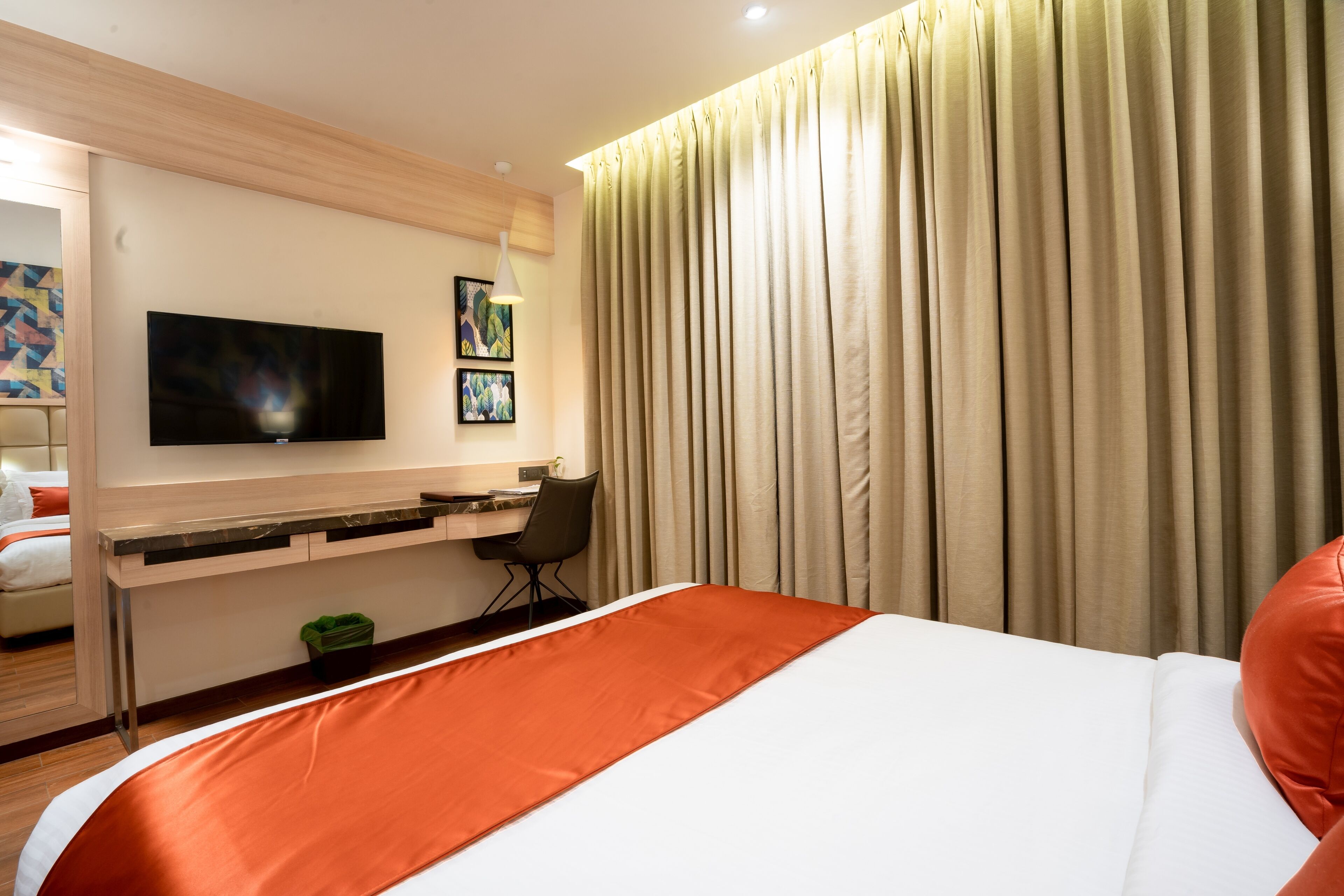Una habitación de hotel con una cama, un escritorio con una silla, un televisor y cortinas.