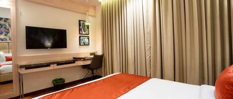 Una habitación de hotel con una cama, un escritorio con una silla, un televisor y cortinas.