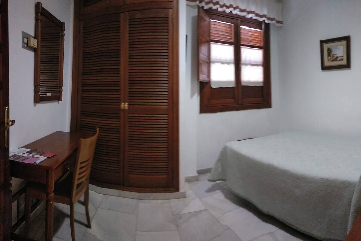 A bedroom with a bed, a desk, and a wardrobe.
