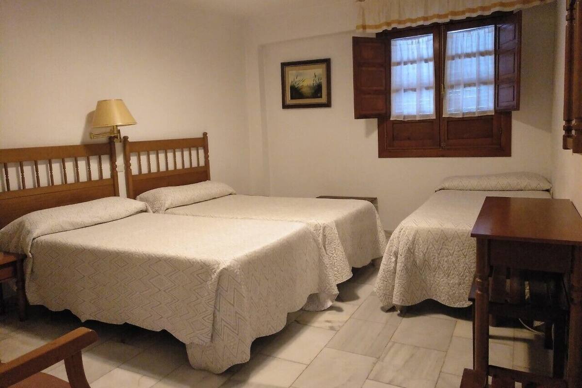 A bedroom with two beds, a wooden headboard, a bedside table, a lamp, and a window with curtains.