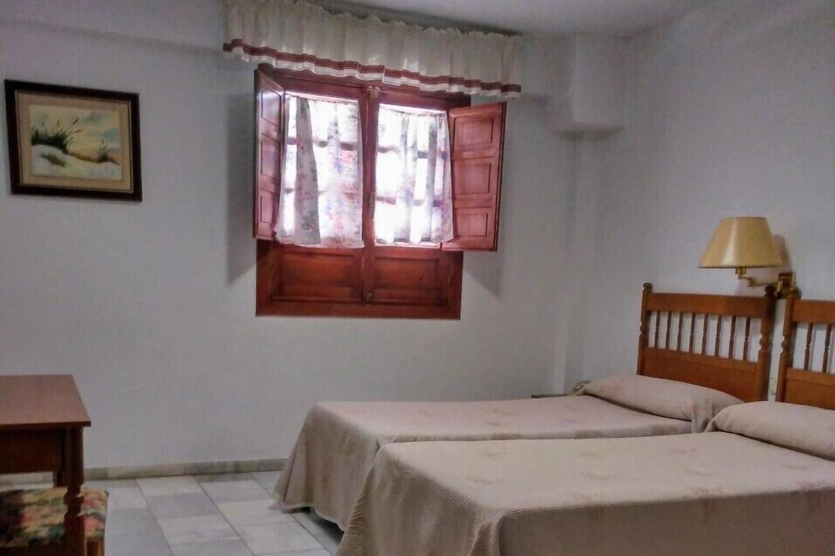 A bedroom with two beds, a wooden nightstand, a table, and a window with curtains.