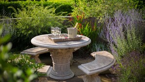 A garden setting with a stone table, two benches, and a tray with glasses and a bottle. - The Dovecote Barns (York)
