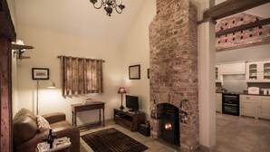 A cozy living room with a fireplace, a sofa, a coffee table, and a television. - The Dovecote Barns (York)