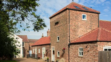 A traditional brick building with a red-tiled roof, multiple windows, and a small tower-like structure.