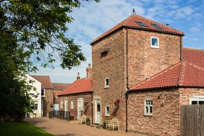 A traditional brick building with a red-tiled roof, multiple windows, and a small tower-like structure.