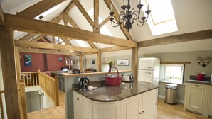 A spacious kitchen with wooden beams, a large island, and a view to a balcony. - The Dovecote Barns (York)