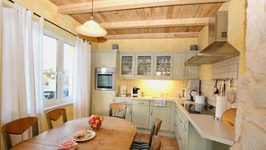 A cozy kitchen with wooden cabinets, a dining table with chairs, and a window with curtains. - Haus Krabbe (Göhren)
