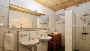 Un baño moderno con dos lavamanos, un mueble de tocador de madera, un espejo grande y una cabina de ducha.