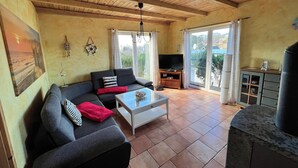 A living room with a sofa, a coffee table, a TV, and a view through large windows. - Haus Krabbe (Göhren)