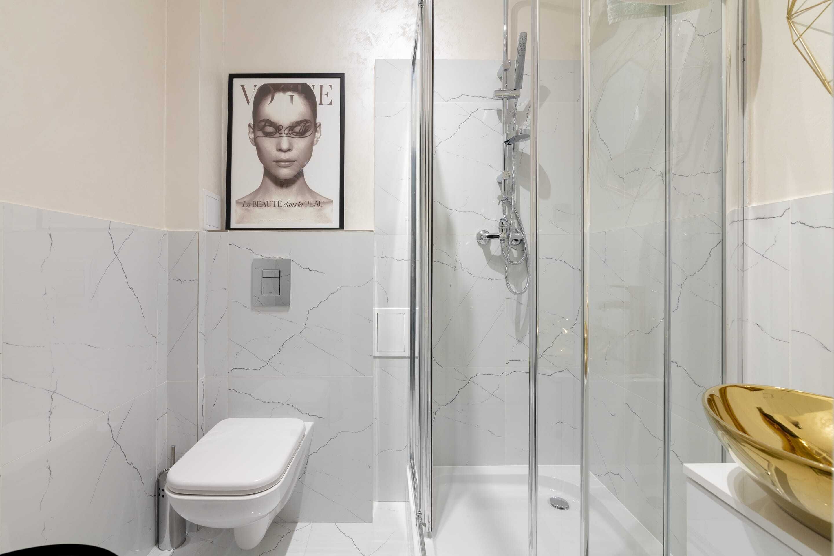 Un baño moderno con ducha envuelta en vidrio, inodoro y pared con azulejos de mármol.