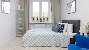 Ein modernes Schlafzimmer mit einem Bett, einem Glastisch, einem Fenster mit Pflanzen und einem gerahmten Bild an der Wand.
