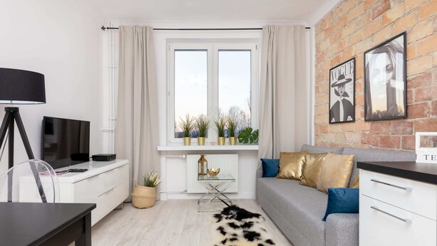 Ein modernes Wohnzimmer mit einer Couch, einem Couchtisch, einem Fernseher und einem Fenster mit Vorhängen.