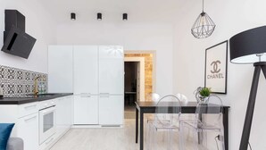 Eine moderne Küche mit weißen Schränken, einer schwarzen Arbeitsplatte und einem Essbereich mit transparenten Stühlen und einem schwarzen Tisch.