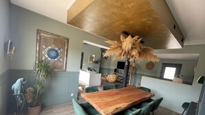 A dining area with a wooden table and green upholstered chairs, a large mirror, and a decorative plant.