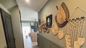 A hallway with wooden flooring, a wall decorated with woven wall hangings, and a macrame piece.