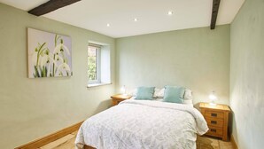 A bedroom with a bed, two bedside tables, a window, and a painting on the wall. - Snowdrop Cottage (Knaresborough)