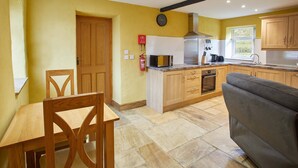 A kitchen with a wooden table and chairs, a microwave, a stove, and wooden cabinets. - Snowdrop Cottage (Knaresborough)