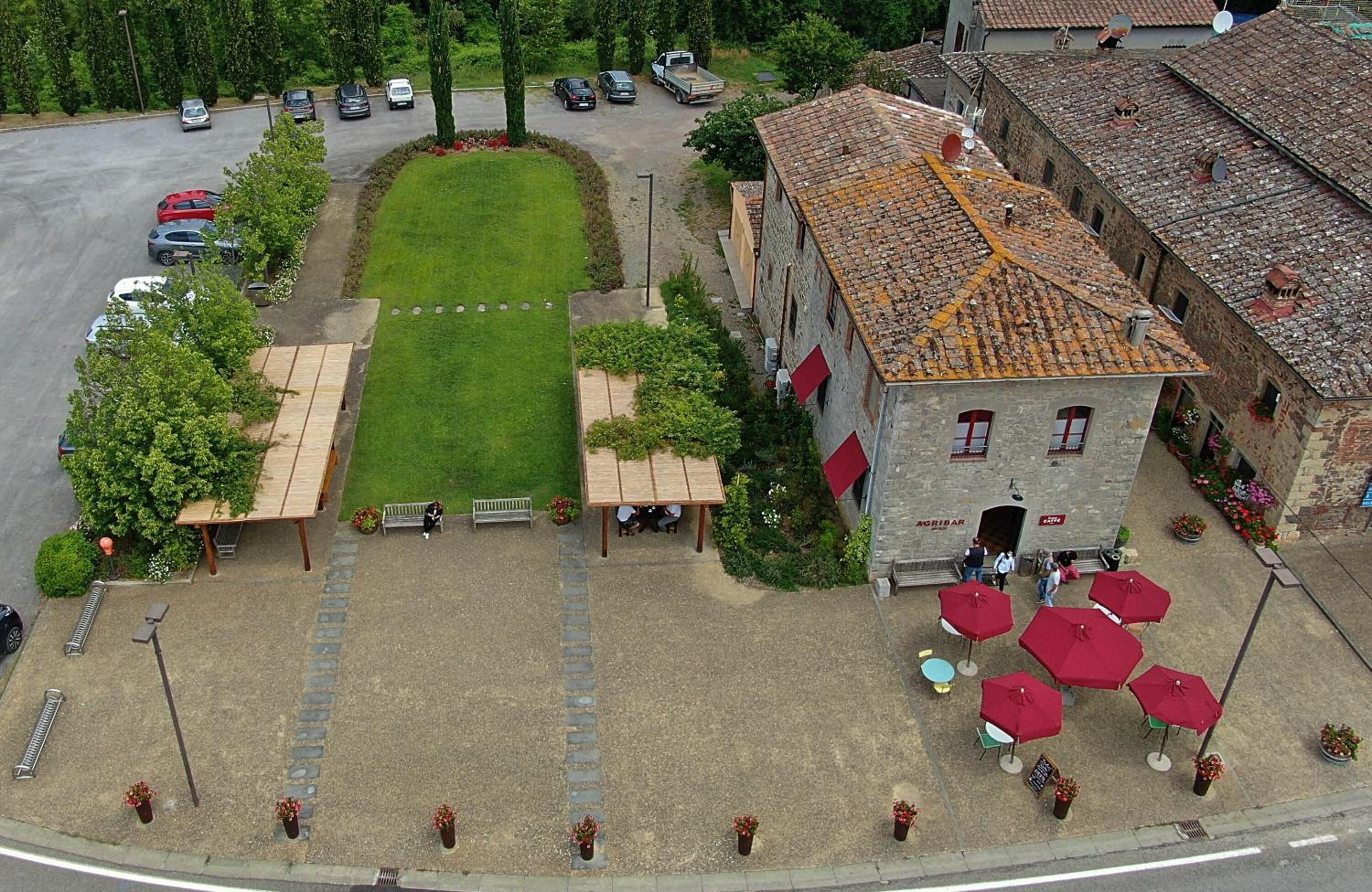 Un área de estar al aire libre con mesas y sombrillas, un patio empedrado y un edificio con techo de tejas.