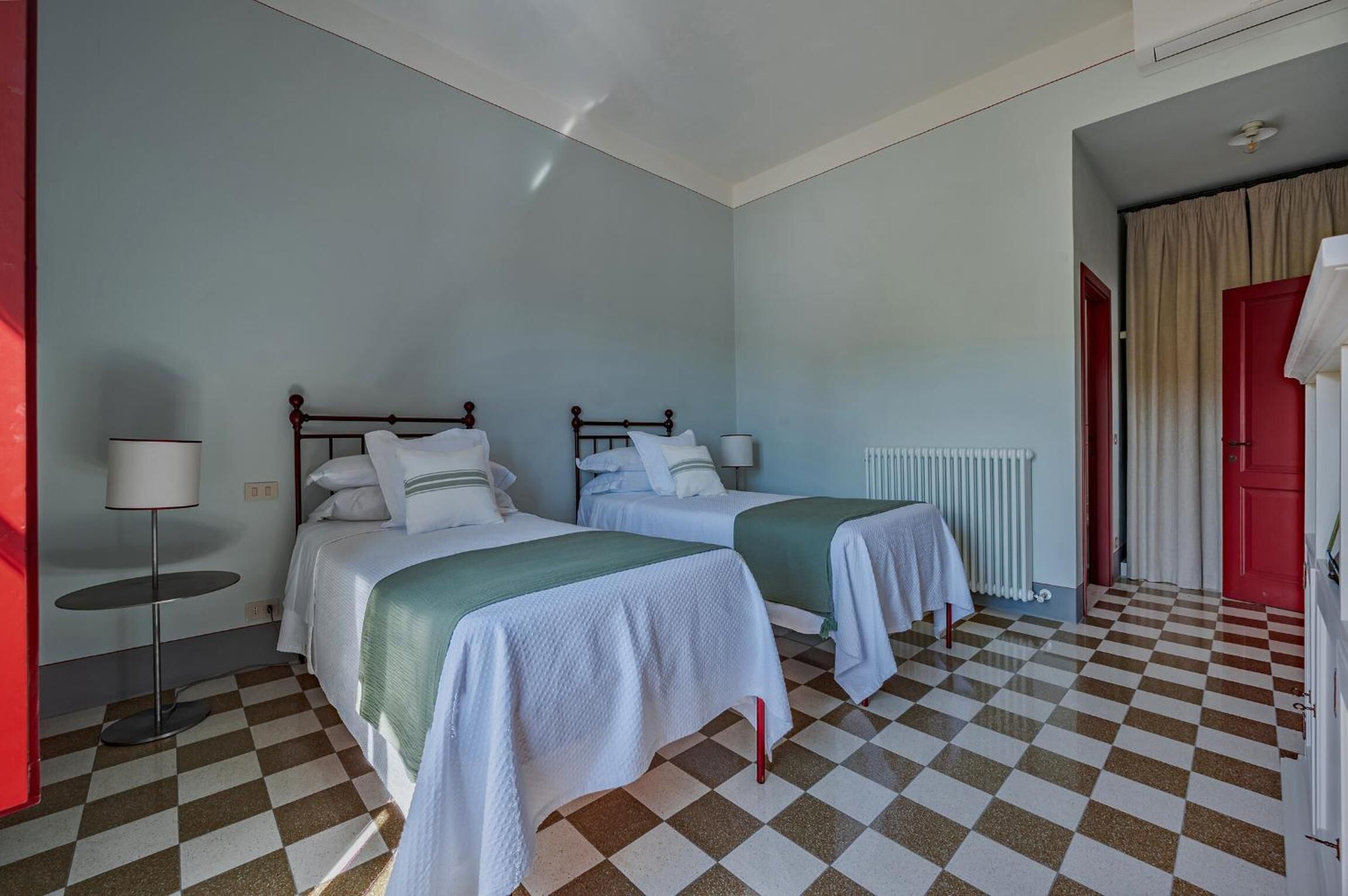 Una habitación con dos camas, un radiador, una mesa y un suelo a cuadros.