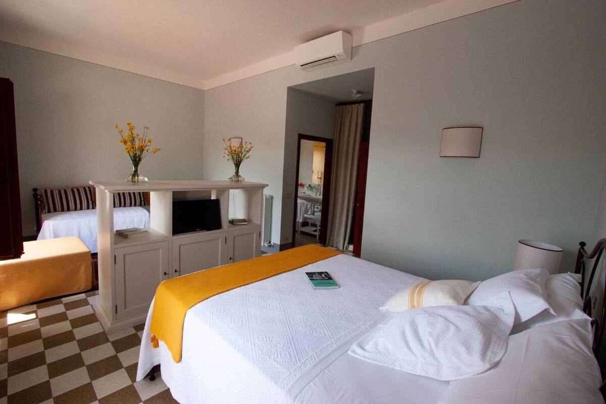A hotel room with a bed, a desk with a computer, a chair, and a small table with a vase of flowers.