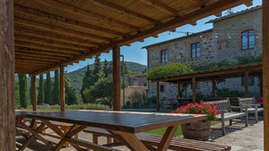 An outdoor patio with wooden tables and benches, stone buildings in the background, and a clear view of the surrounding landscape. - Brolio Agriroom (Gaiole in Chianti)