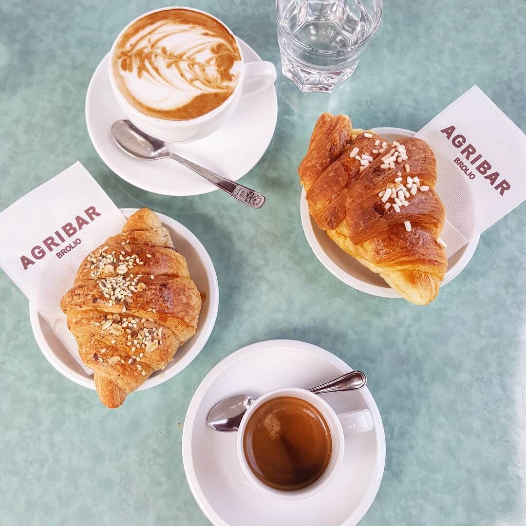 Una mesa con una taza de café, un vaso de agua y dos croissants que dicen "AGRIBAR BROLIO".
