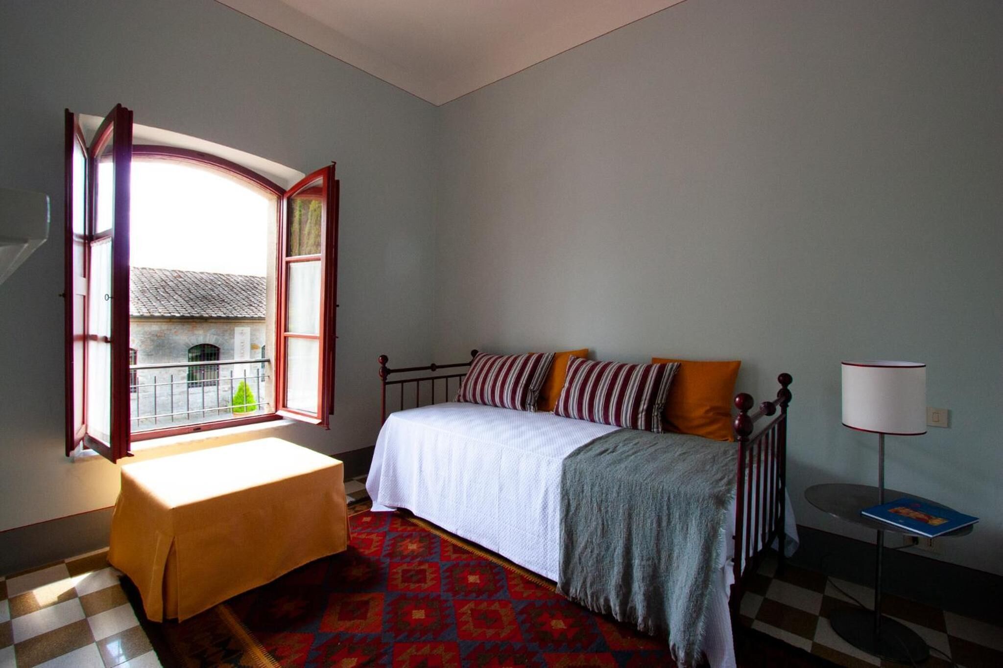 Un dormitorio con cama, una mesa, una lámpara y una ventana con vistas a un edificio.