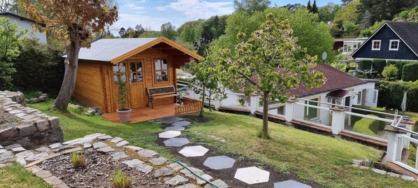 Una cabaña de madera con un porche, un camino de piedra y un árbol pequeño.
