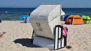 Una playa con una silla de mimbre blanca, un paraguas azul y tiendas de colores.