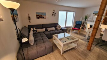 Una sala de estar con un sofá modular, una mesa de centro de vidrio y un comedor con una silla y una mesa.