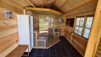A wooden cabin interior with a white refrigerator, a wooden bench, and a glass door leading to an outdoor area.
