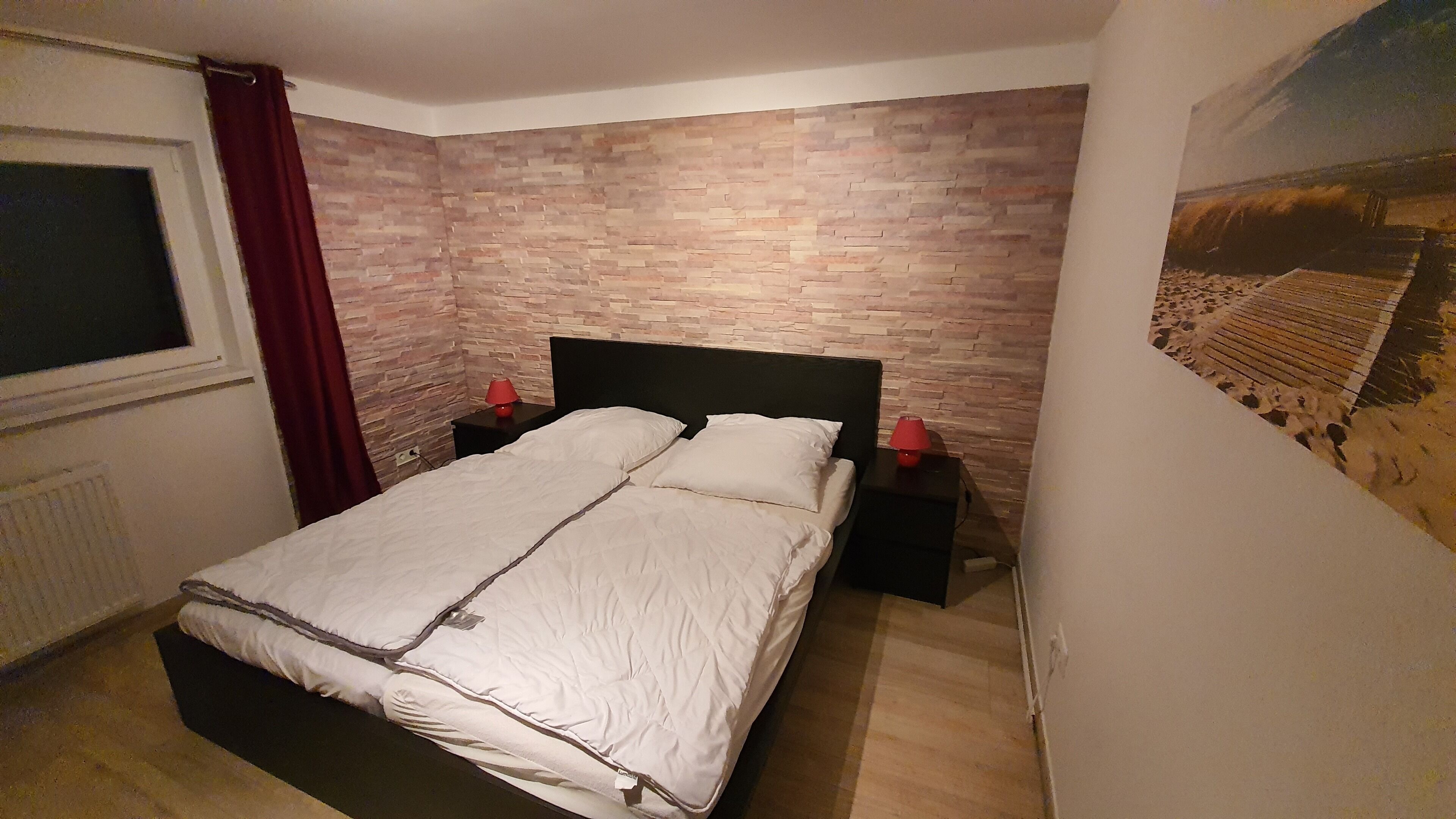Una camera da letto con parete decorata a mattoni, un letto con biancheria bianca, due comodini con lampade e una finestra con tenda.
