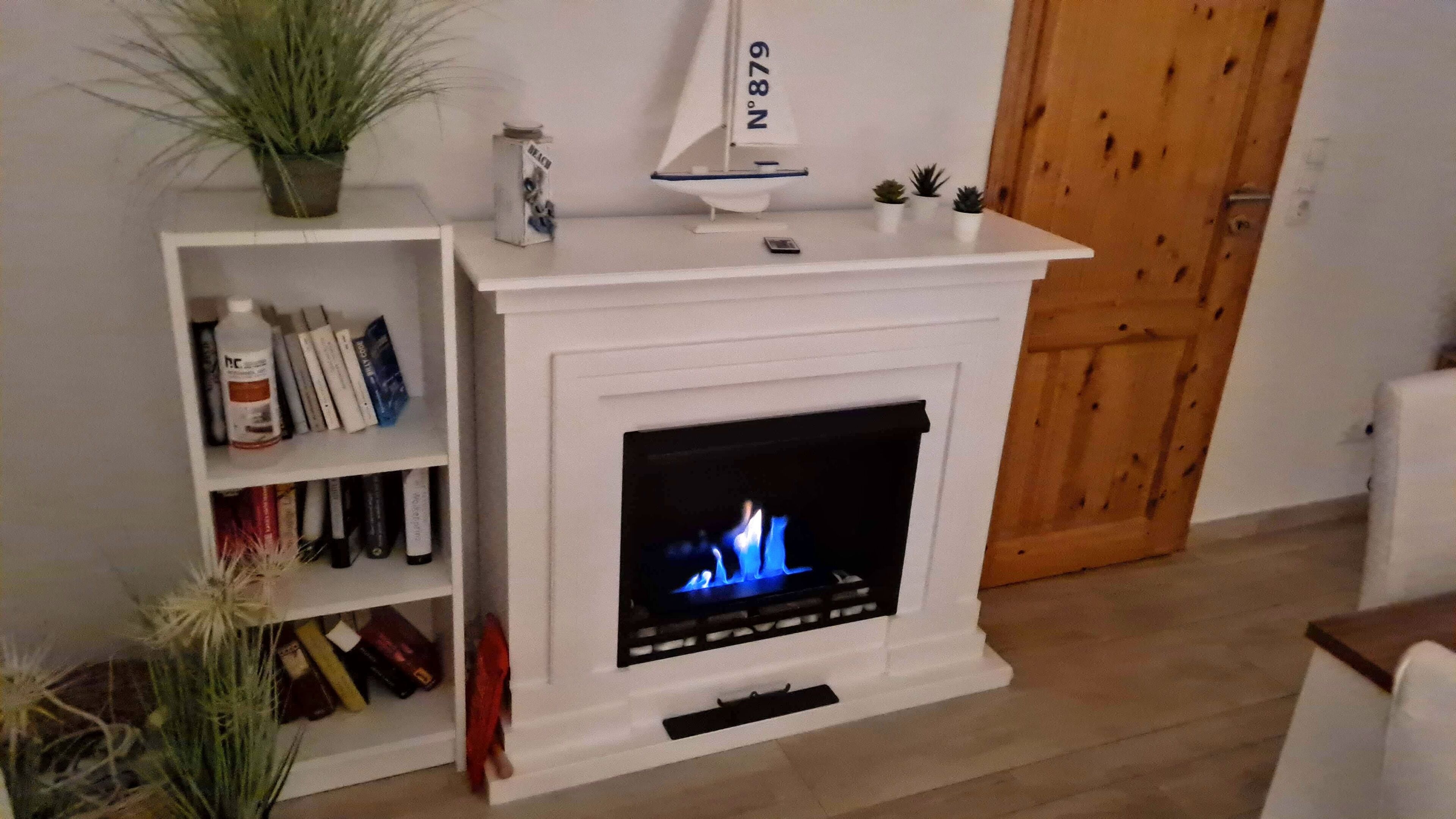 Een woonkamer met een witte schoorsteen, een boekenkast en een klein model zeilboot.