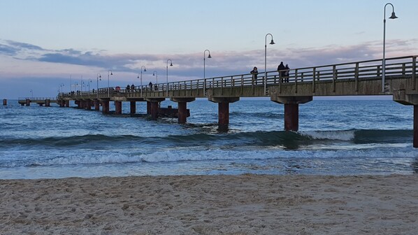 Un muelle se adentra en el mar, con una playa de arena en primer plano.