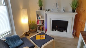 Ett mysigt vardagsrum med en öppen spis, en bokhylla och en bekväm sittgrupp.