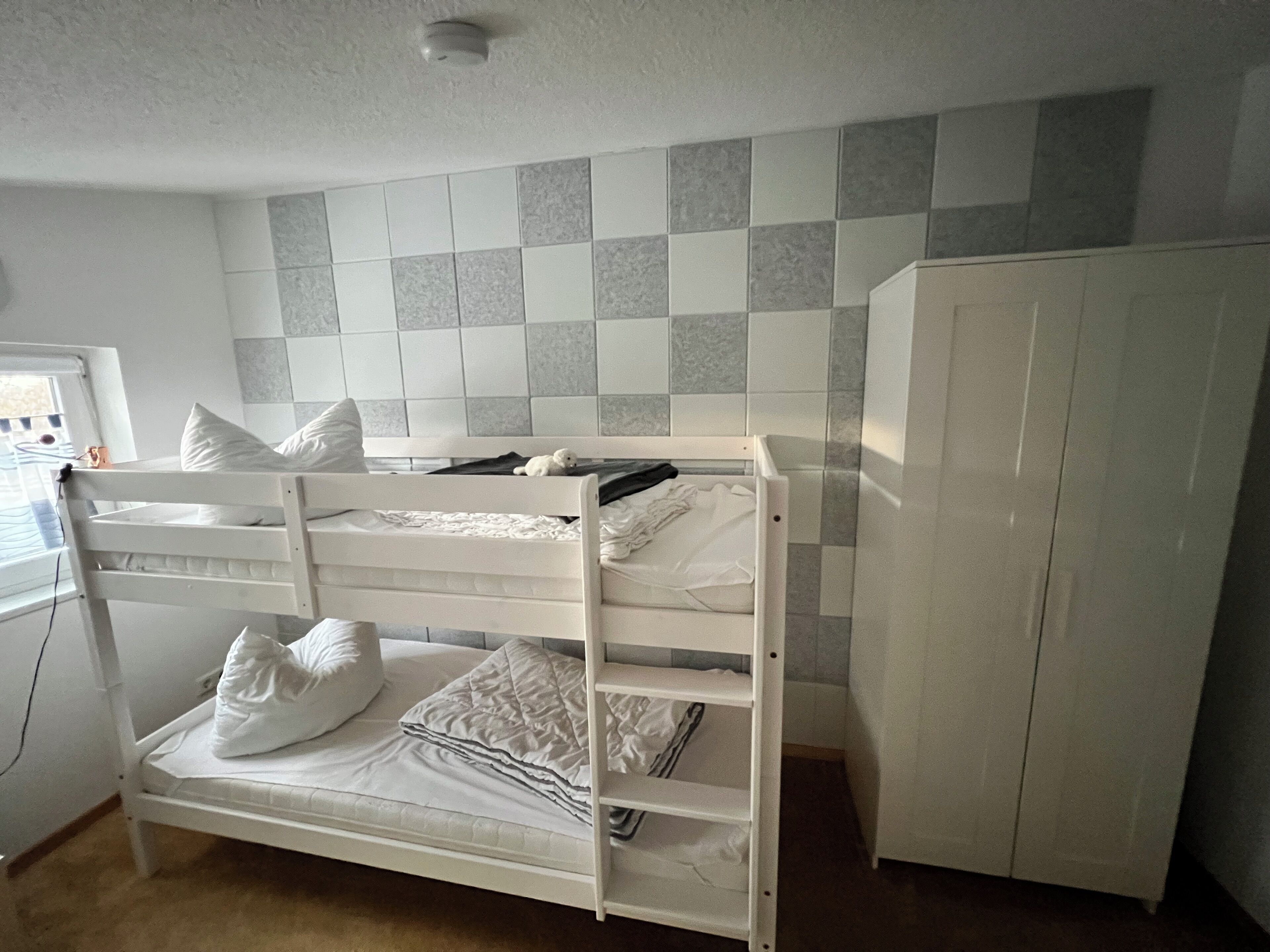 A bunk bed with white bedding and pillows, a wardrobe, and a tiled wall.