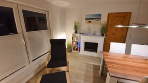 Ett modernt vardagsrum med en öppen spis, en bokhylla och en matplats med ett träbord och stolar.