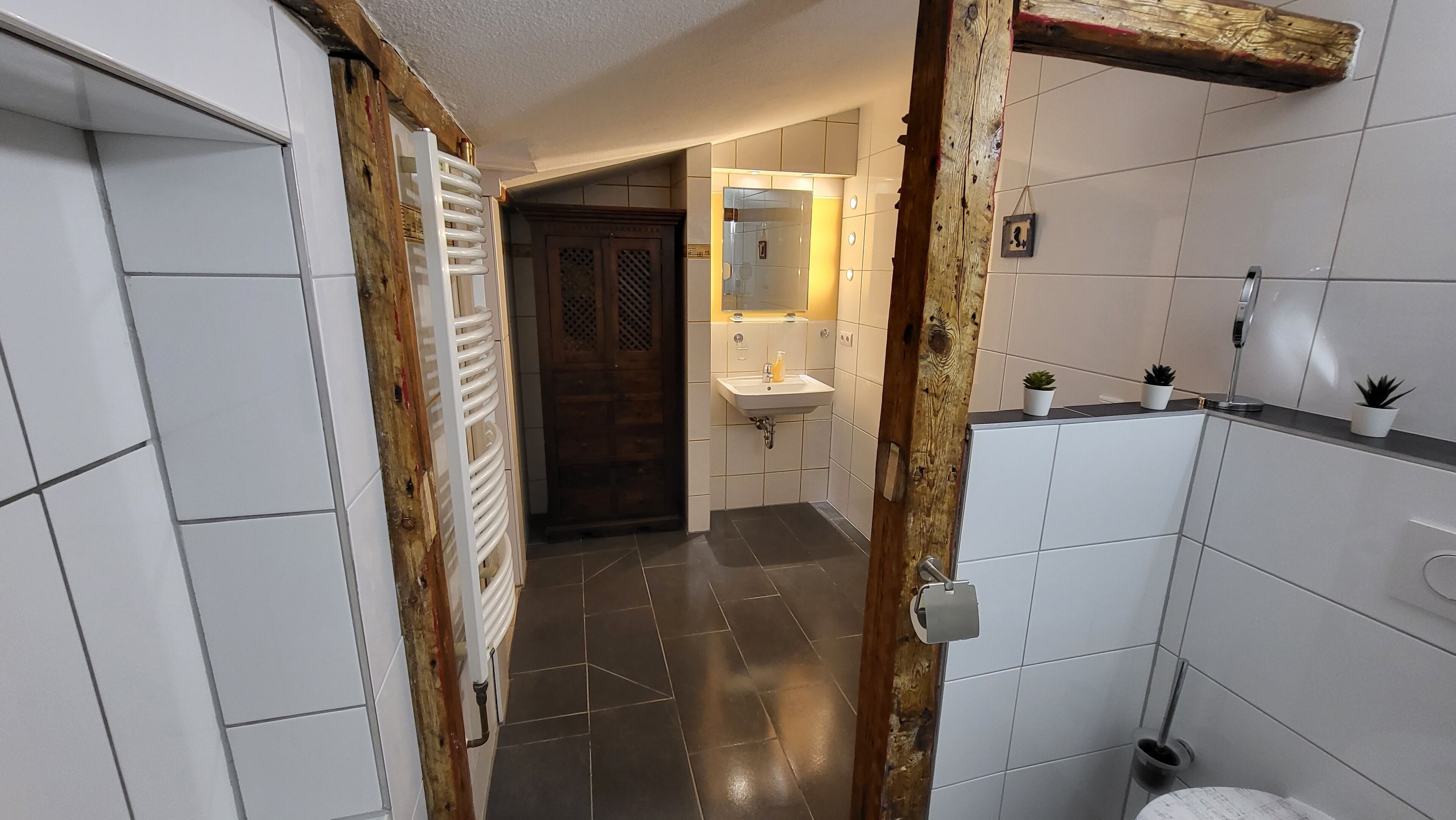 A narrow hallway with a wooden door, a white radiator, and a sink with a mirror above it.