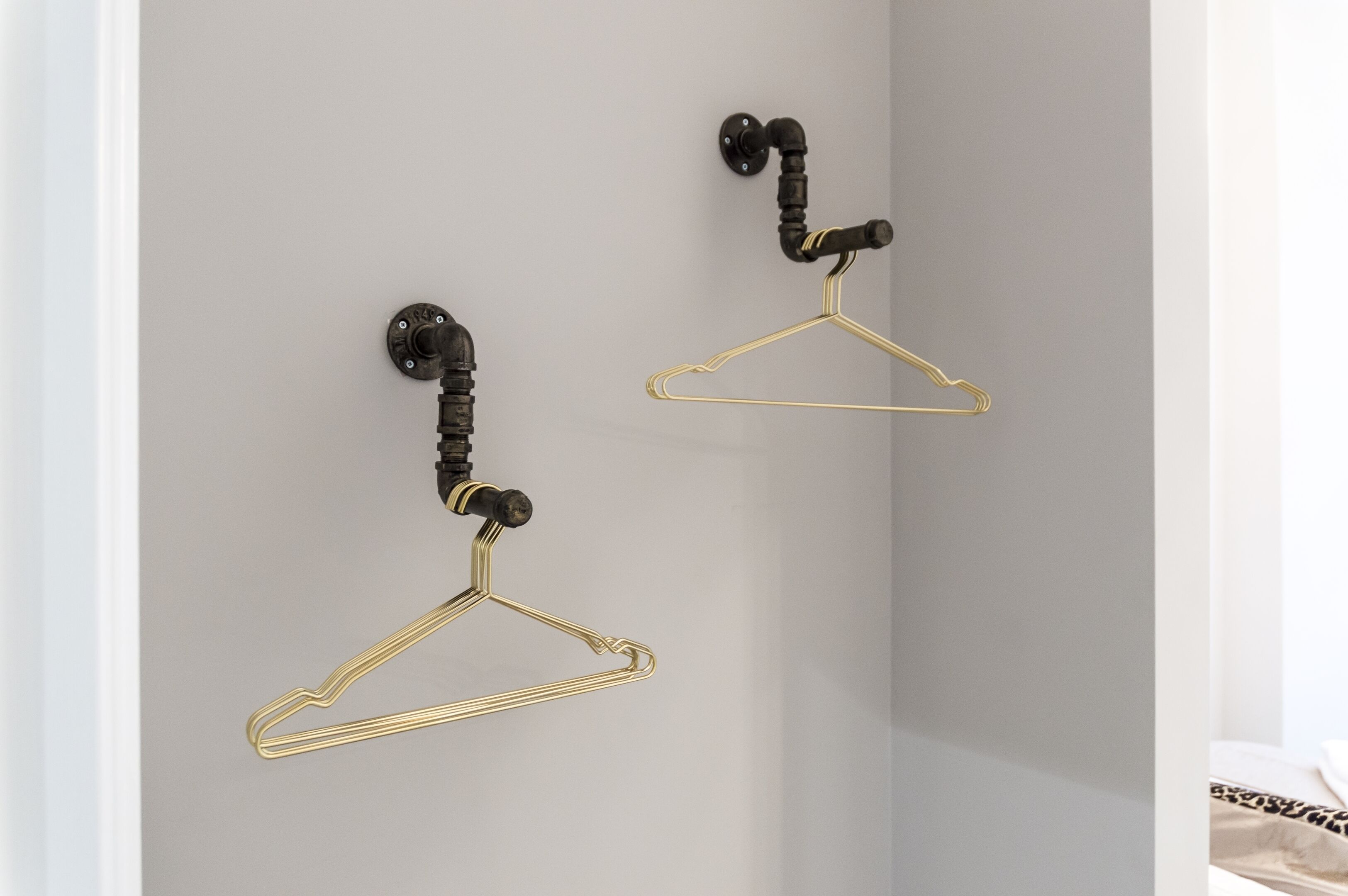Deux porte-manteaux dorés à fixer au mur, avec des poignées noires.