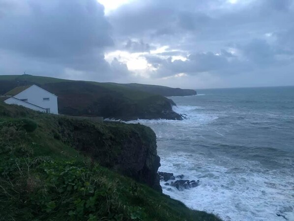 A coastal scene with a white building on a grassy cliff overlooking the sea.