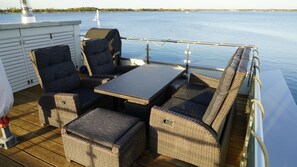 A deck with wicker furniture, a table, and chairs, overlooking a calm body of water.