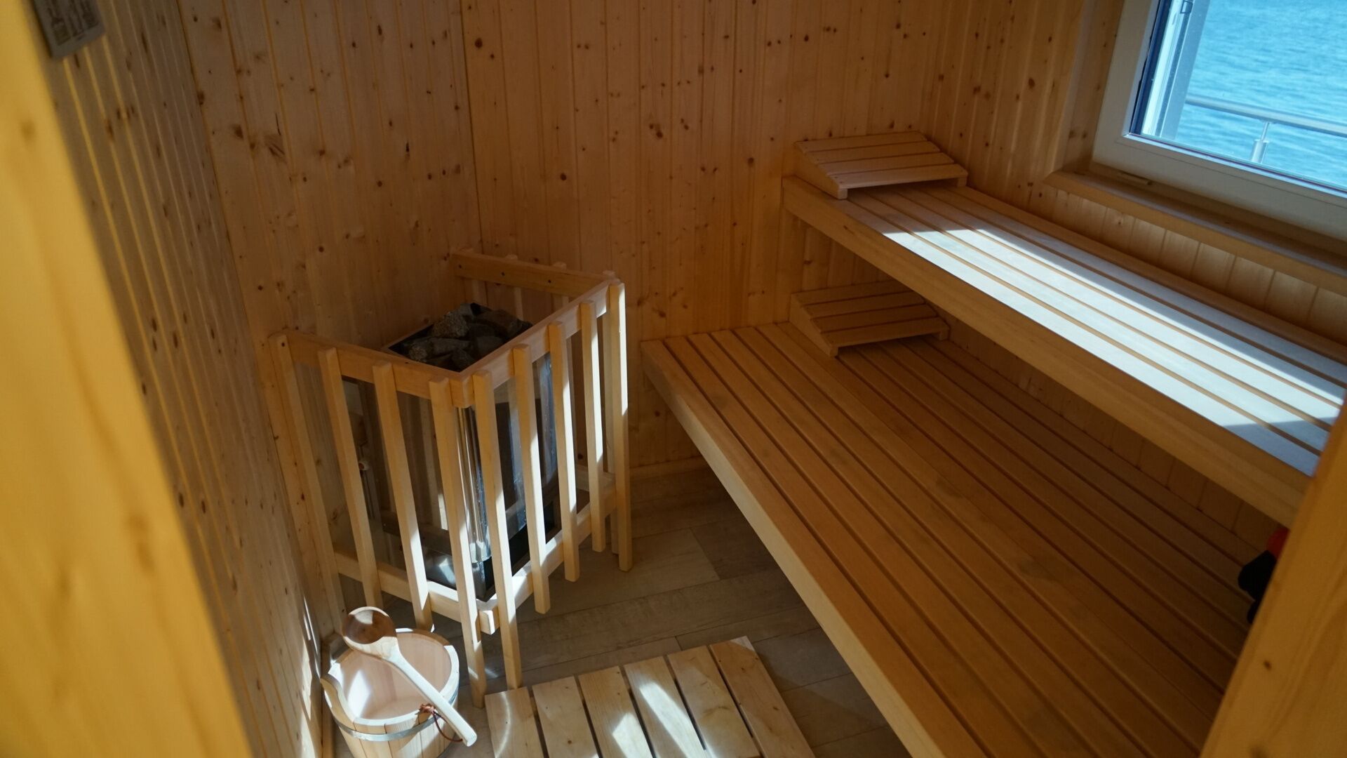 A sauna room with wooden benches, a wooden bench with a window, and a sauna tub.