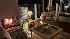 A cozy living room with a fireplace, a comfortable armchair, a glass coffee table, and a ship model on a shelf.