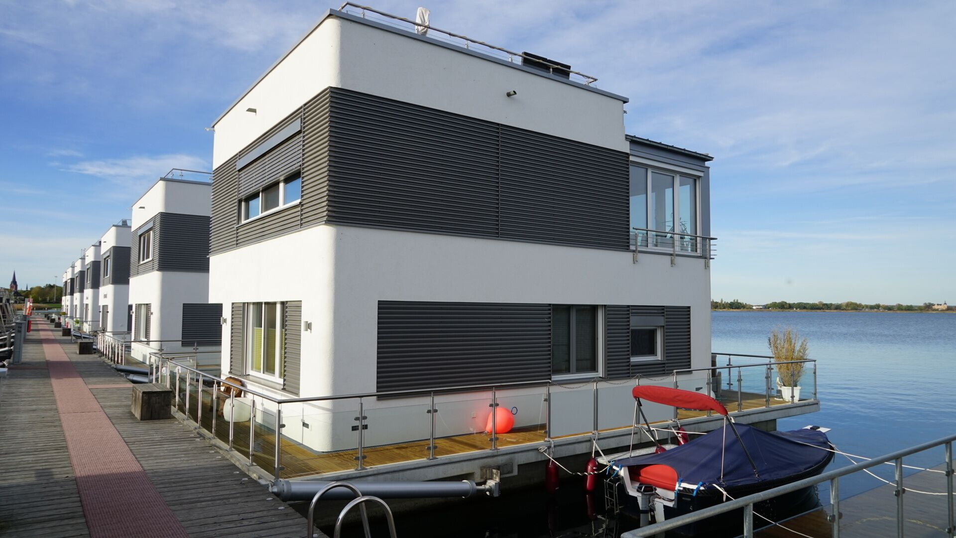 A modern multi-story building with a flat roof, large windows, and a dock extending into a body of water.
