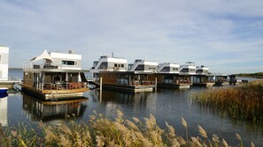 A series of modern floating homes with open decks and large windows, situated on calm water with a clear sky.
