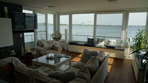 A spacious living room with a large window overlooking a body of water, a fireplace, and a cozy seating area.