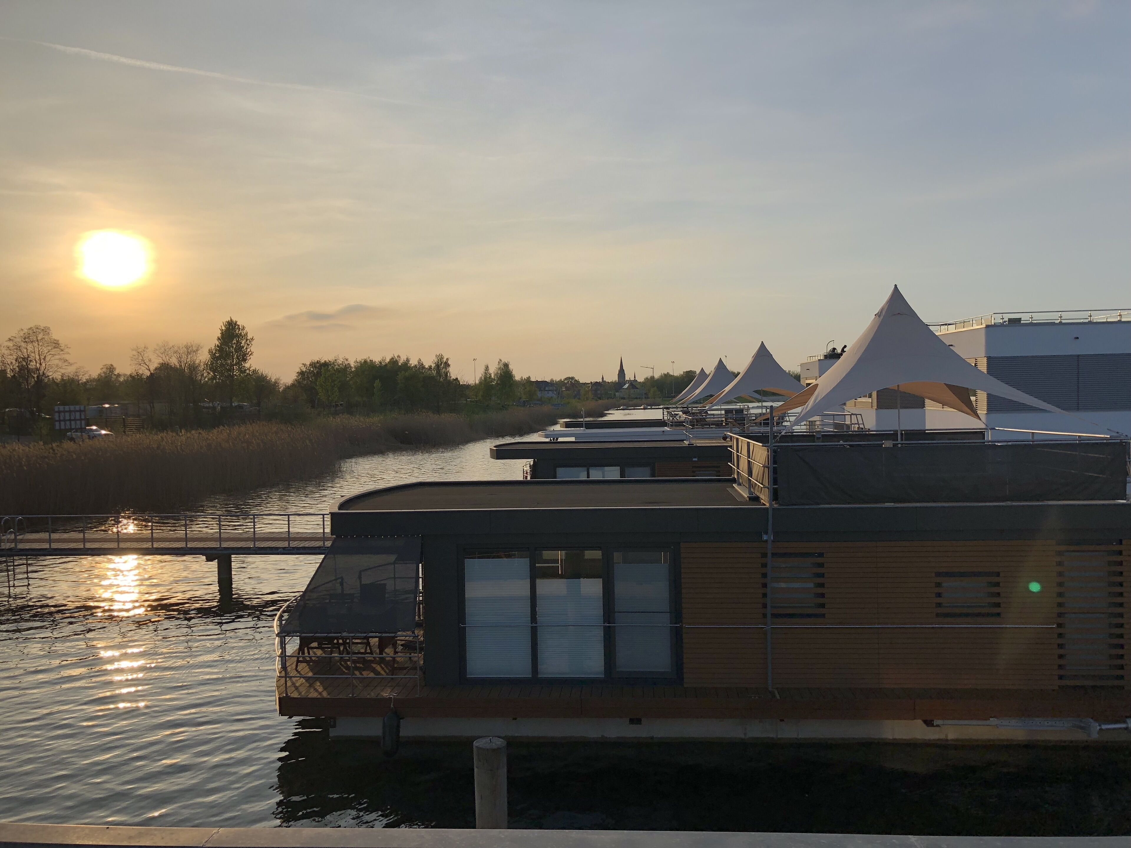 A riverside building with a wooden facade and a glass window, surrounded by tents and a calm river.