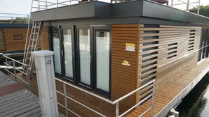 Un edificio moderno con fachada de madera y ventanas amplias, cerca de una masa de agua.